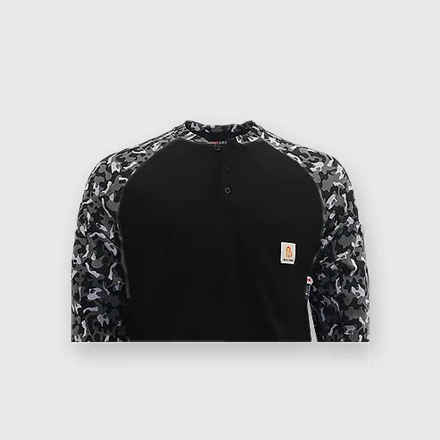 A worker wearing a Bocomal FR camouflage t-shirt with buttons, standing in front of industrial equipment.