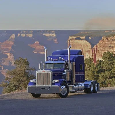 A classic purple Peterbilt truck parked with a scenic backdrop of California-like mountains.